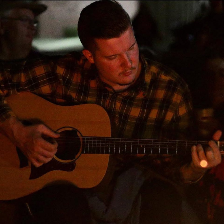 Daniel playing guitar in warm low light
