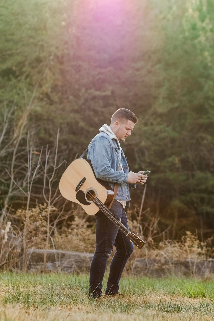 Daniel with guitar in a sunlit field