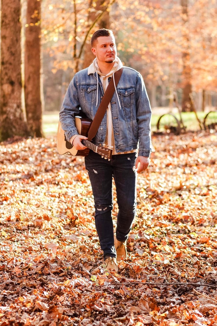 Daniel walking through autumn leaves with his guitar