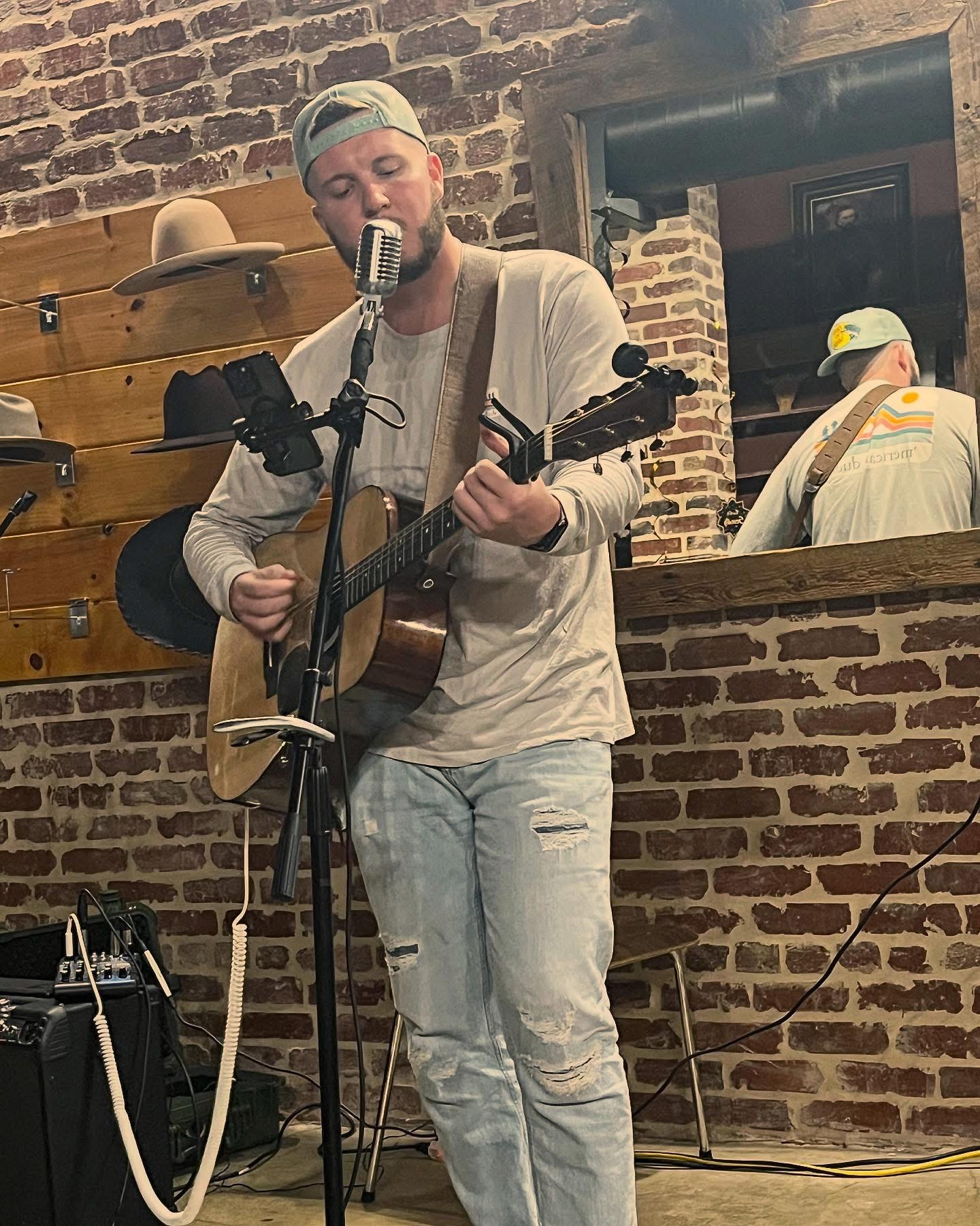 Daniel singing with guitar against a brick wall